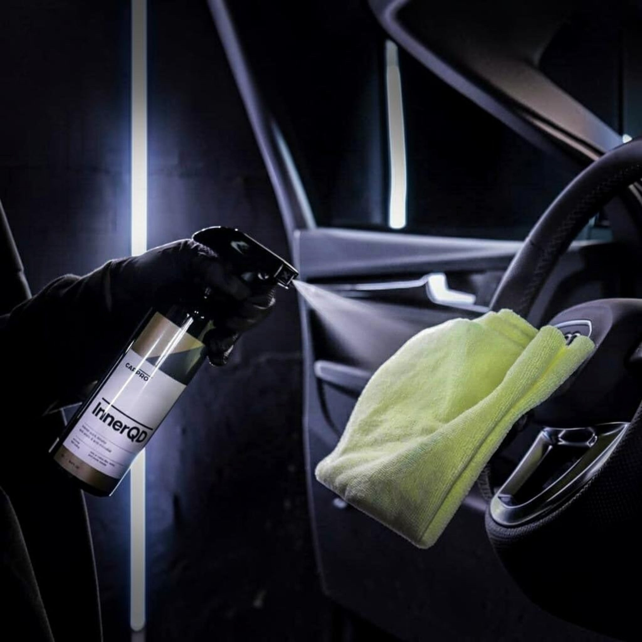 Planet Car Care CarPro InnerQD interior quick detailer spray being applied to a car steering wheel with a microfiber cloth