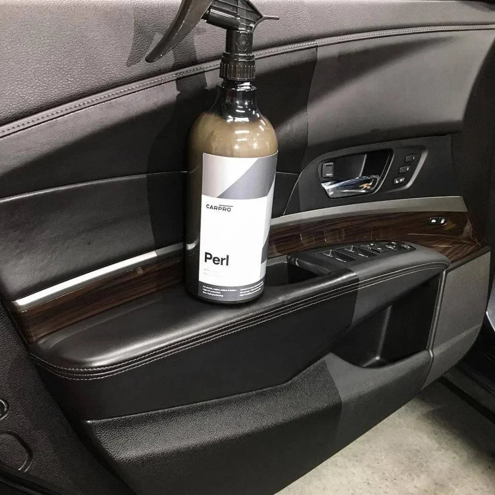 Planet Car Care CarPro Perl 1L bottle resting on a car door panel to demonstrate interior plastic and leather care.