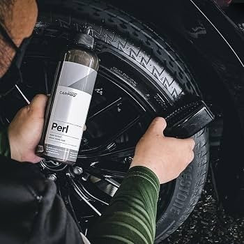 Planet Car Care user applying CarPro Perl water-based dressing to a car tire with a detailing brush for UV protection.