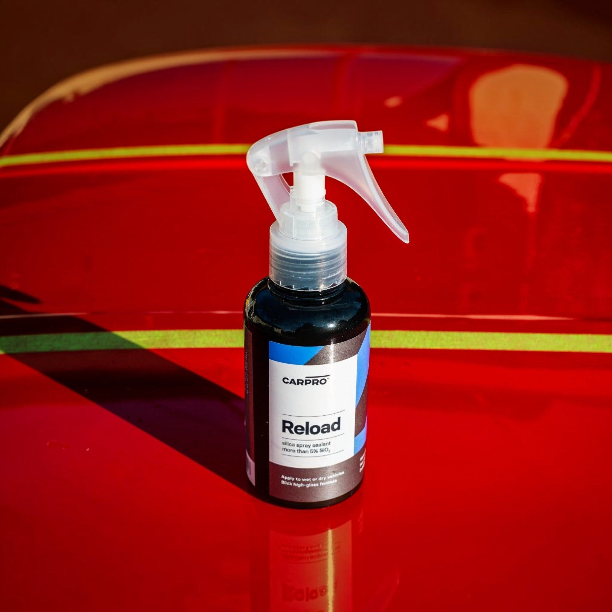 Planet Car Care CarPro Reload 2.0 silica spray sealant in a 100ml bottle resting on a glossy red car hood.