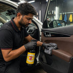 A professional detailer using Planet Car Care ClearPro APC to clean a car door panel with a microfiber cloth.