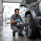 Planet Car Care technician in grey uniform spraying cleaner on a car wheel in a professional auto detailing studio