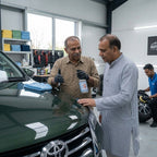 Planet Car Care Eco Gloss waterless wash spray being used by two men to clean a green car in a professional garage